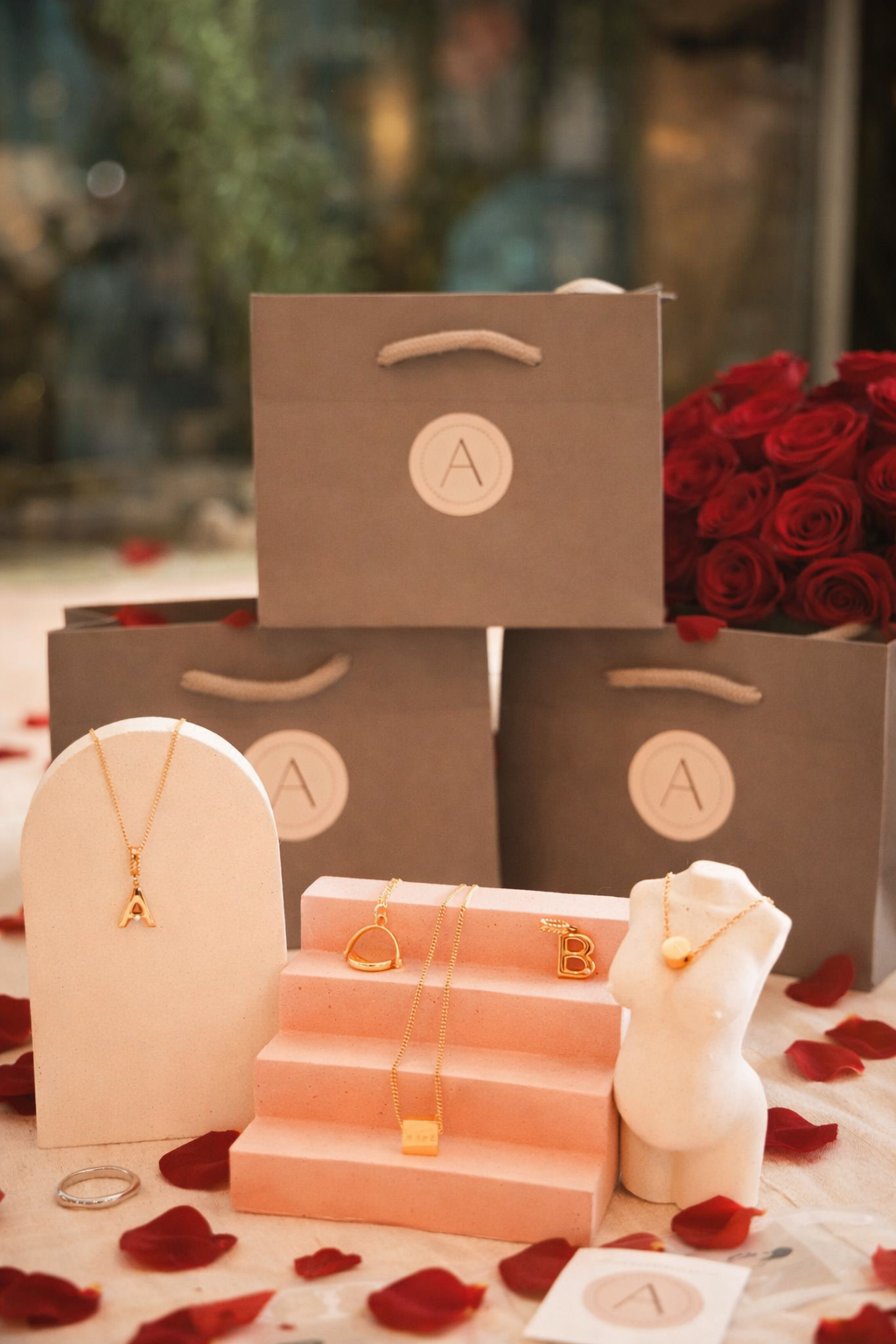 Jewelry display with necklaces on stands, gift bags, and red roses in the background.